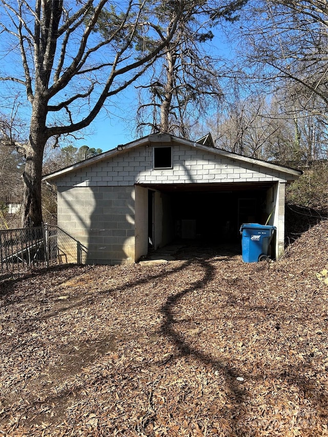 garage featuring dirt driveway, a carport, and fence