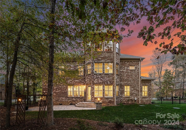 back house at dusk featuring a lawn