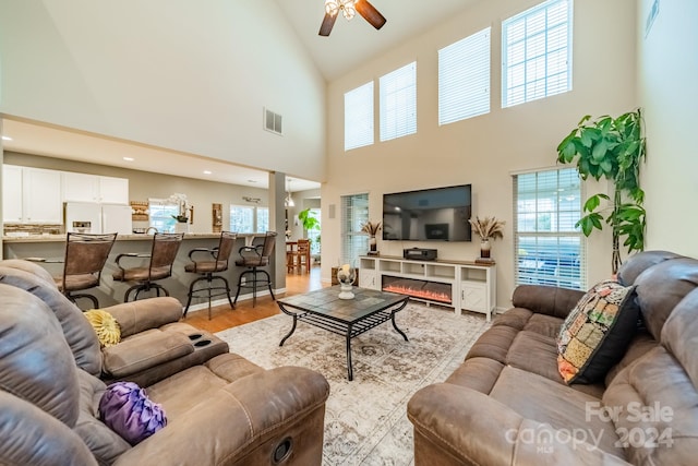 living room featuring ceiling fan, high vaulted ceiling, and light hardwood / wood-style flooring