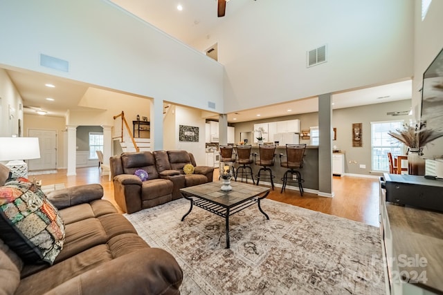 living room featuring ceiling fan, decorative columns, high vaulted ceiling, and light hardwood / wood-style flooring