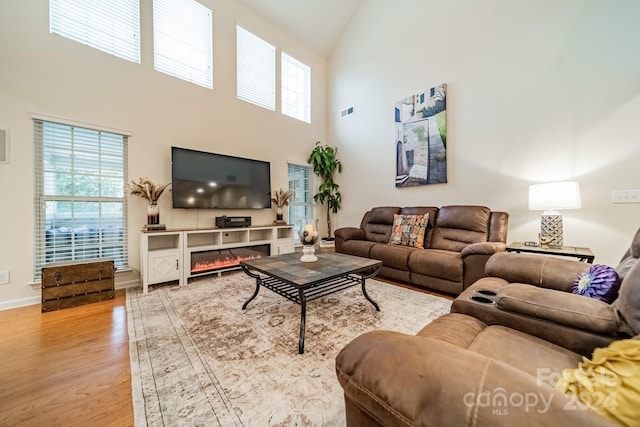 living room with plenty of natural light, a towering ceiling, and light hardwood / wood-style floors