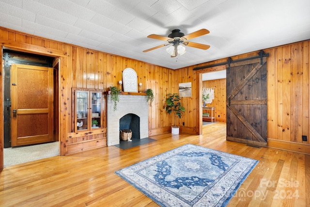 living room with hardwood / wood-style floors, ceiling fan, wooden walls, and a barn door