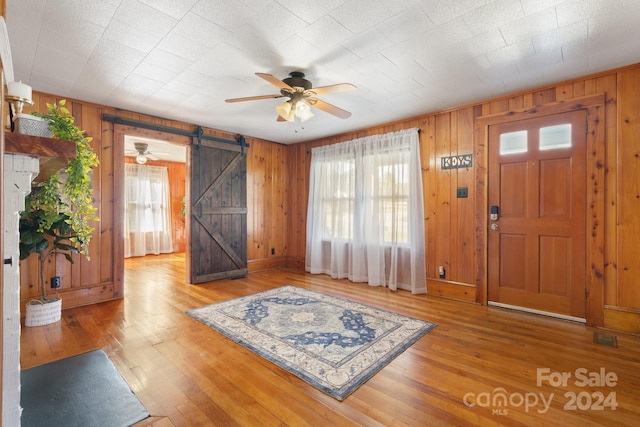 foyer with wood-type flooring, a barn door, ceiling fan, and wooden walls