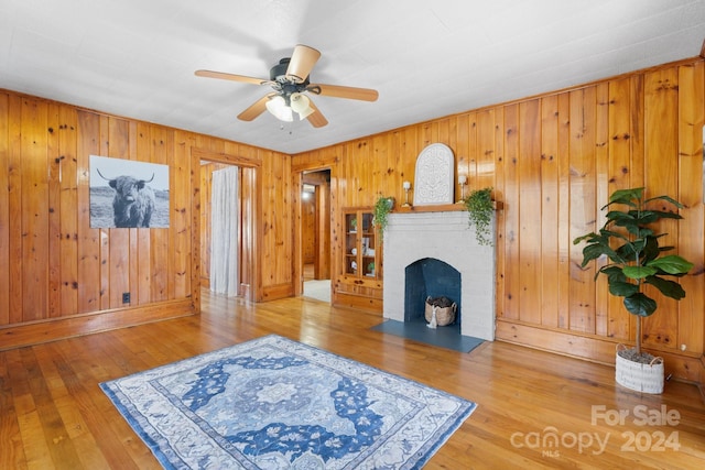 living room with wooden walls, a fireplace, ceiling fan, and wood-type flooring