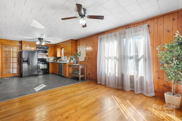 kitchen featuring hardwood / wood-style flooring, ceiling fan, wood walls, and black appliances