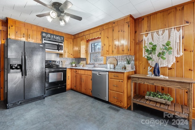 kitchen with backsplash, ceiling fan, black appliances, and wood walls