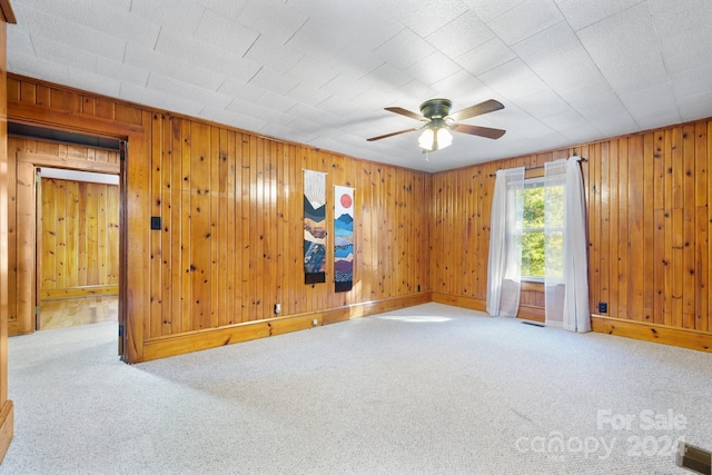 carpeted spare room with wood walls and ceiling fan