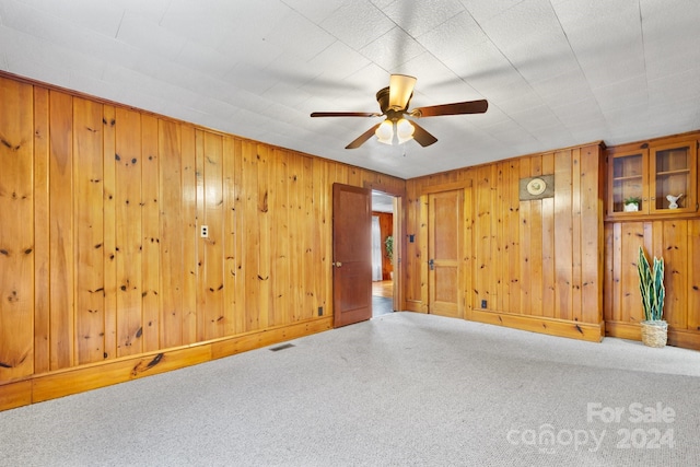 unfurnished room with wood walls, ceiling fan, and carpet floors