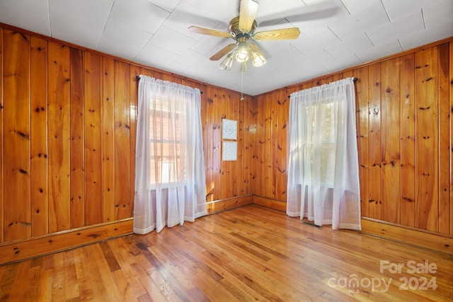 spare room featuring light wood-type flooring, ceiling fan, and wooden walls