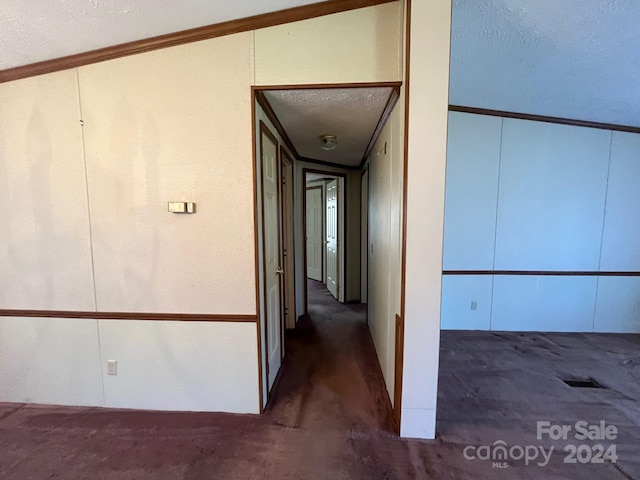 hall featuring vaulted ceiling, dark carpet, a textured ceiling, and ornamental molding