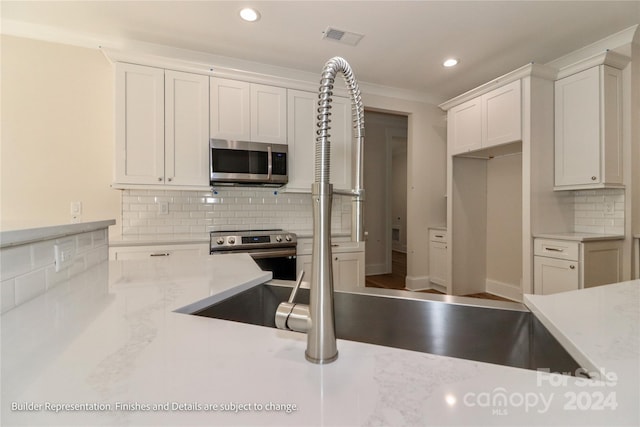 kitchen featuring white cabinetry, stainless steel appliances, light stone counters, crown molding, and decorative backsplash