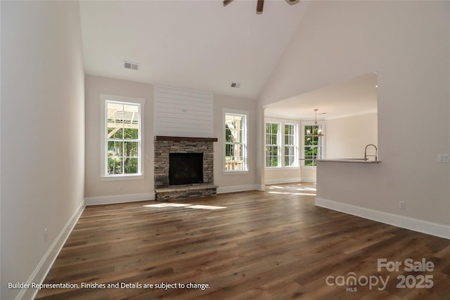 unfurnished living room with a stone fireplace, visible vents, baseboards, and wood finished floors