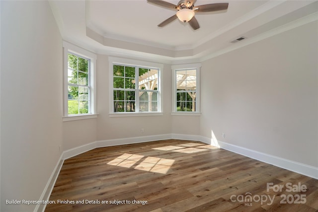spare room with wood finished floors, visible vents, ornamental molding, and a tray ceiling