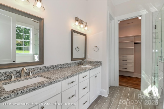 bathroom with a shower stall, wood finished floors, a sink, and double vanity