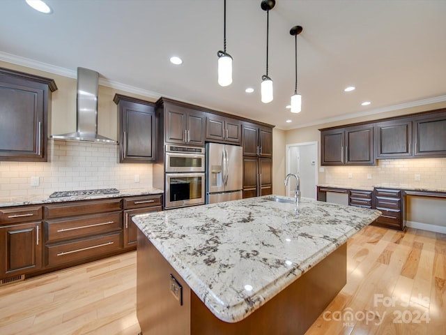 kitchen with wall chimney exhaust hood, stainless steel appliances, and a kitchen island with sink