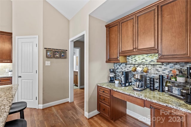 169 Rimmer Farm Rd, Troutman, NC 28166 - kitchen with decorative backsplash, brown cabinetry, light wood-type flooring, light stone counters, and baseboards