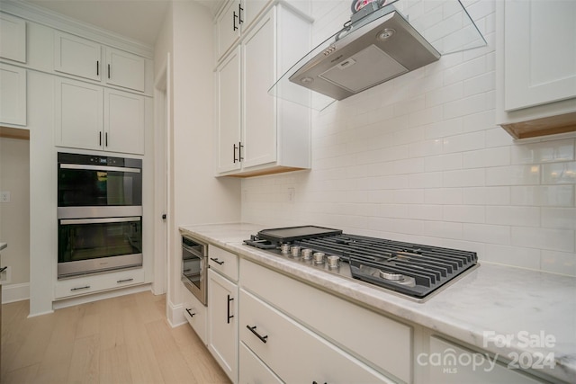 kitchen featuring backsplash, exhaust hood, stainless steel appliances, and light wood-type flooring