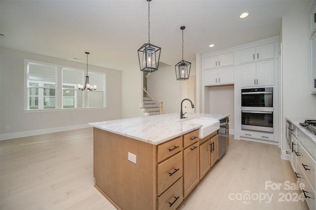 kitchen with appliances with stainless steel finishes, a kitchen island with sink, sink, light hardwood / wood-style flooring, and white cabinets