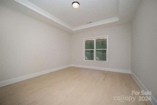 empty room featuring a raised ceiling, crown molding, and light wood-type flooring