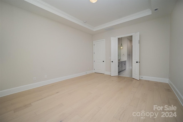 unfurnished bedroom with light hardwood / wood-style floors, ornamental molding, and a tray ceiling