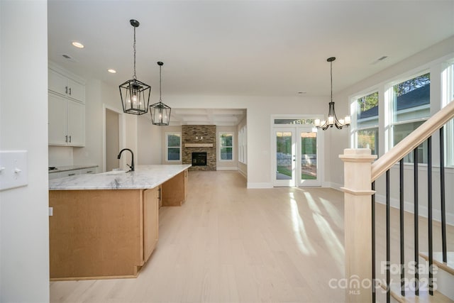 kitchen with a large island, hanging light fixtures, open floor plan, white cabinetry, and light stone countertops