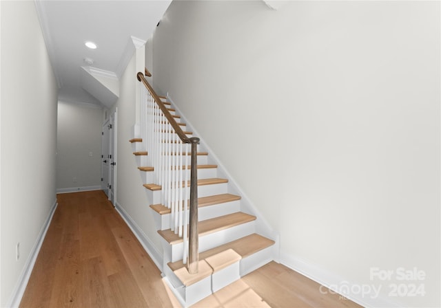 stairway with wood-type flooring and crown molding