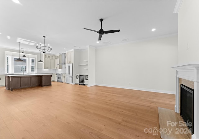 unfurnished living room featuring ceiling fan with notable chandelier, sink, light wood-type flooring, and ornamental molding