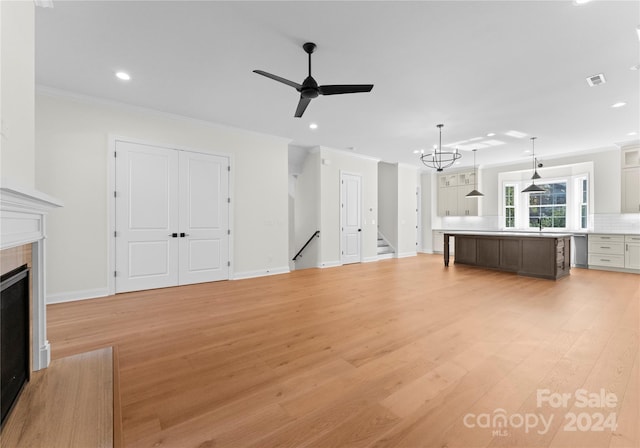 unfurnished living room featuring crown molding, light hardwood / wood-style floors, and ceiling fan with notable chandelier