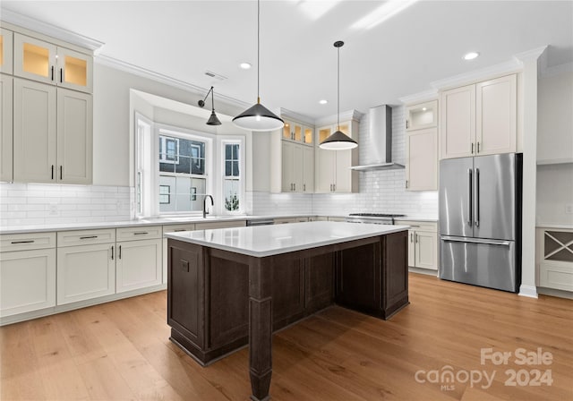 kitchen featuring a center island, crown molding, wall chimney exhaust hood, appliances with stainless steel finishes, and light hardwood / wood-style floors