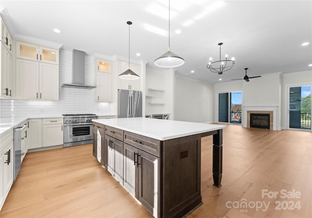 kitchen with hanging light fixtures, a kitchen island, high end appliances, and wall chimney range hood