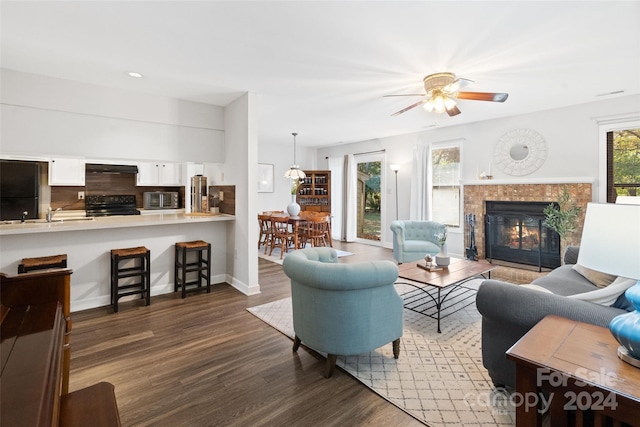 living room featuring ceiling fan, sink, dark wood-type flooring, and a tile fireplace