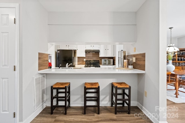 kitchen with a kitchen bar, white cabinets, black appliances, and decorative light fixtures