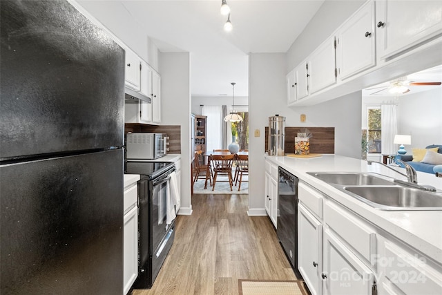 kitchen with sink, black appliances, light hardwood / wood-style flooring, white cabinets, and hanging light fixtures