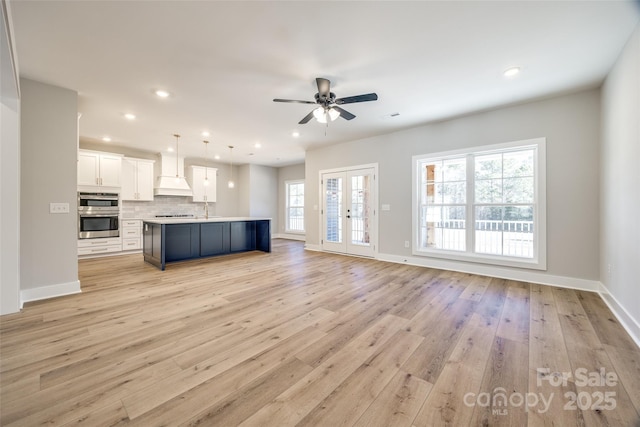 unfurnished living room featuring french doors, sink, ceiling fan, and light hardwood / wood-style flooring