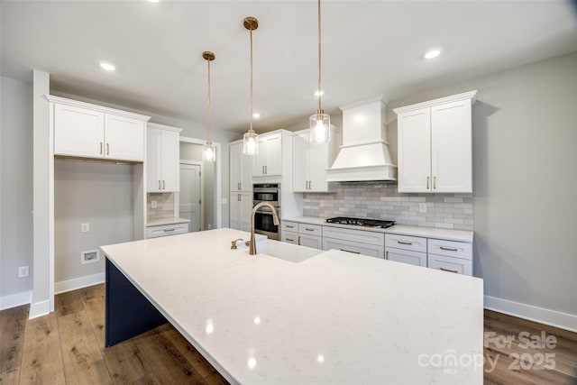 kitchen with premium range hood, hanging light fixtures, gas stovetop, white cabinets, and a center island with sink