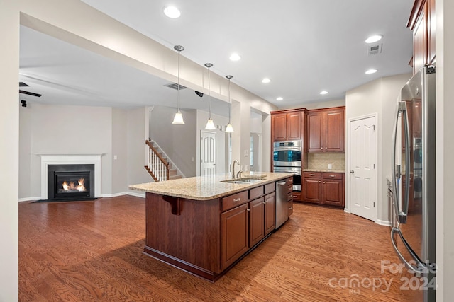 kitchen featuring dark wood-type flooring, a center island with sink, a kitchen breakfast bar, sink, and appliances with stainless steel finishes