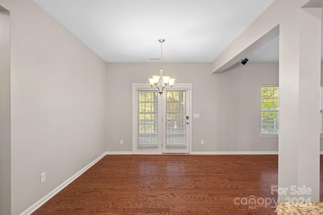 spare room with dark hardwood / wood-style floors, a wealth of natural light, and an inviting chandelier