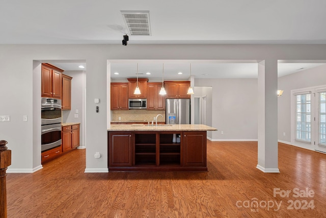 kitchen featuring hardwood / wood-style floors, hanging light fixtures, an island with sink, and stainless steel appliances