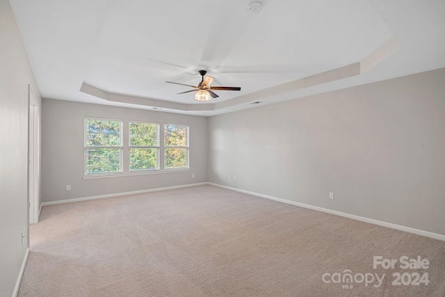 empty room with light carpet, a tray ceiling, and ceiling fan