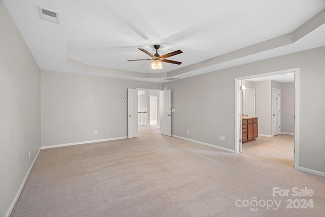 empty room featuring a tray ceiling, ceiling fan, and light colored carpet