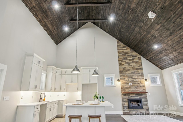 kitchen with high vaulted ceiling, white cabinets, a stone fireplace, hanging light fixtures, and a kitchen island