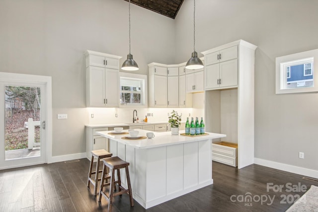 kitchen with white cabinetry, a kitchen island, hanging light fixtures, and dark hardwood / wood-style floors