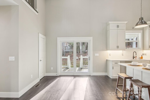 kitchen with sink, hanging light fixtures, dark hardwood / wood-style floors, a towering ceiling, and white cabinetry