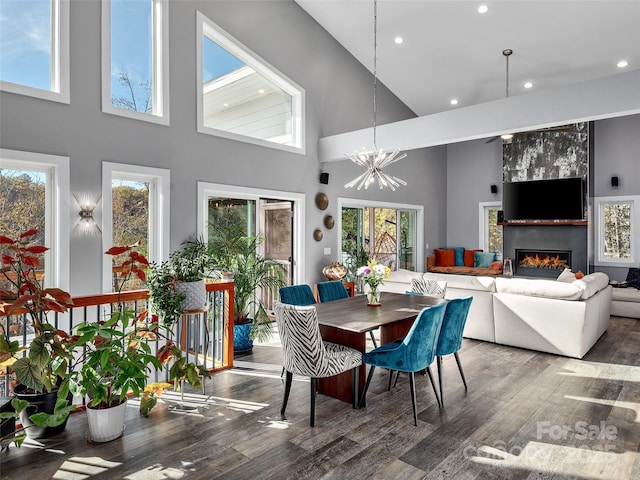 dining space featuring wood-type flooring, a large fireplace, a chandelier, and a towering ceiling