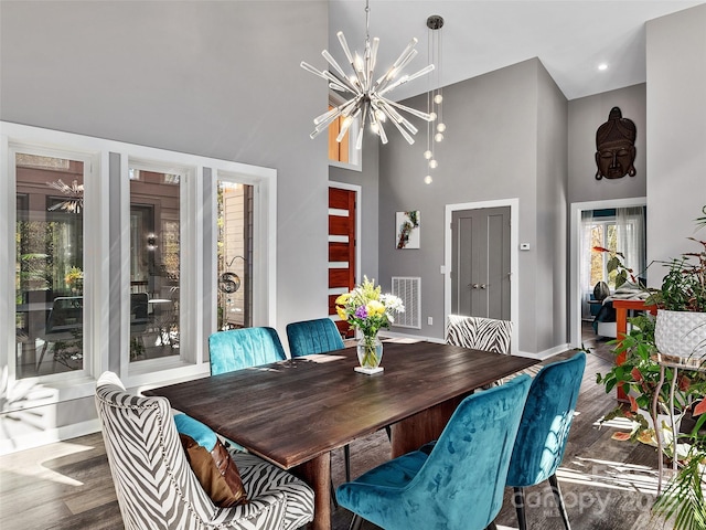 dining area featuring a notable chandelier, wood-type flooring, and a high ceiling