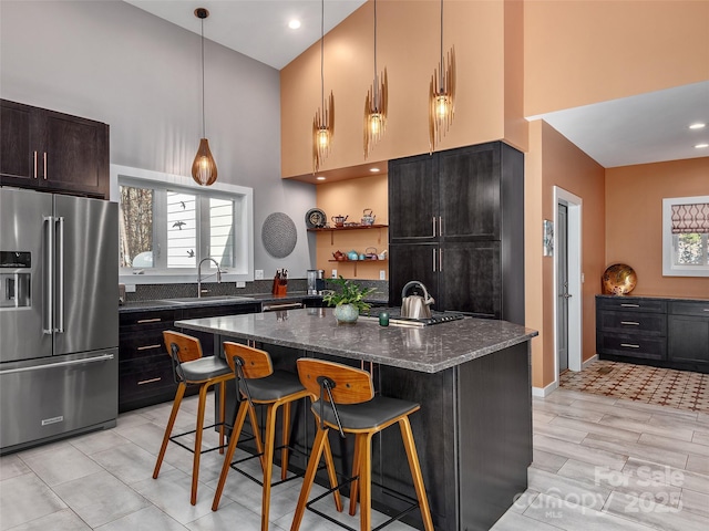 kitchen featuring a towering ceiling, high end fridge, a kitchen island, and dark stone countertops