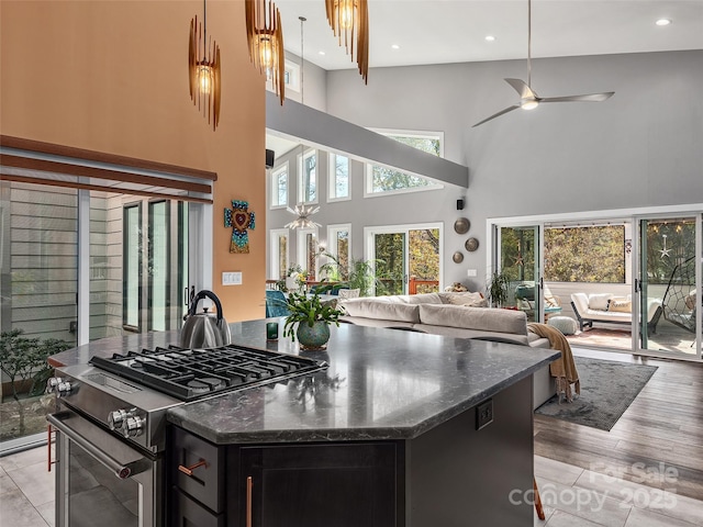 kitchen featuring stainless steel gas range oven, a center island, a towering ceiling, dark stone counters, and light hardwood / wood-style floors