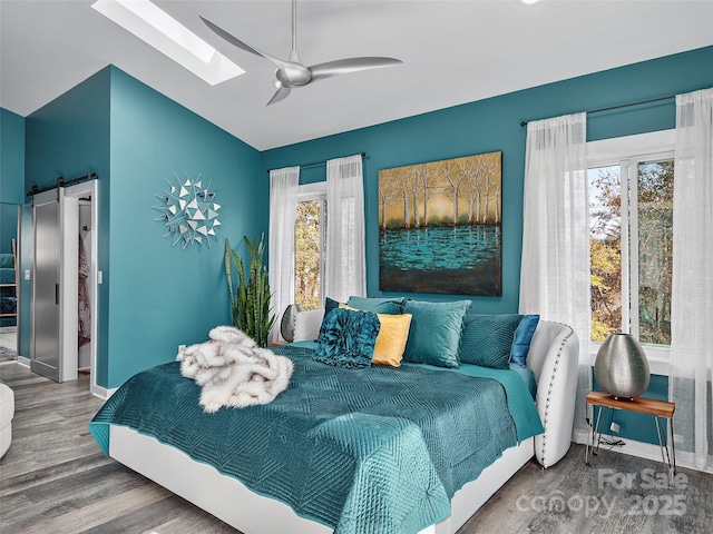 bedroom with ceiling fan, hardwood / wood-style flooring, and vaulted ceiling with skylight