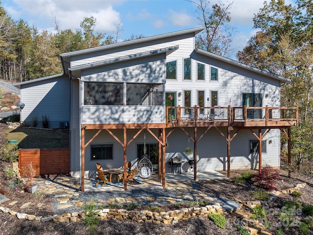 rear view of property featuring a sunroom, a patio area, a deck, and a fire pit