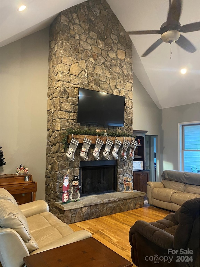 living room featuring wood-type flooring, high vaulted ceiling, a stone fireplace, and ceiling fan